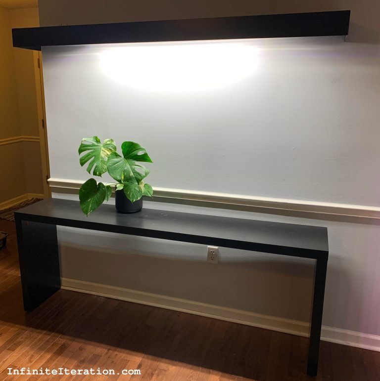 Floating shelf with embedded light shining down on matching table and houseplant